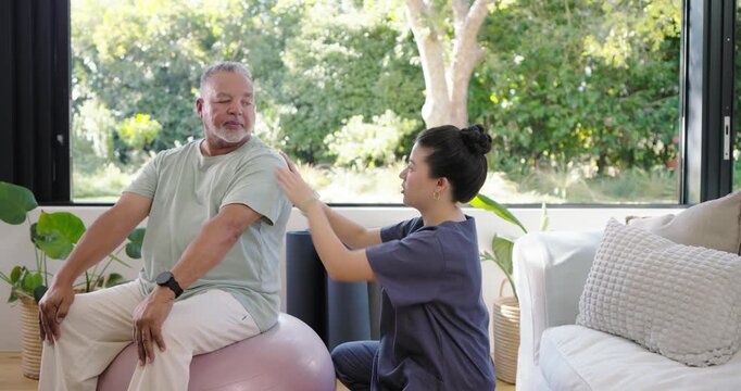Therapist in scrubs palpating shoulder, guiding African American man sitting on pink ball by window