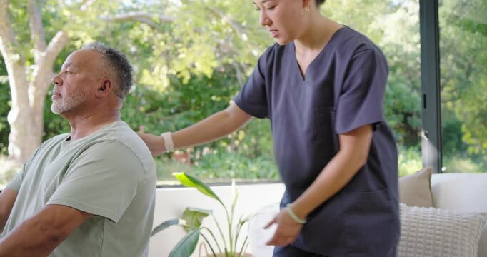 Asian therapist in scrubs speaking, palpating back guiding patient on pink-ball at home for posture