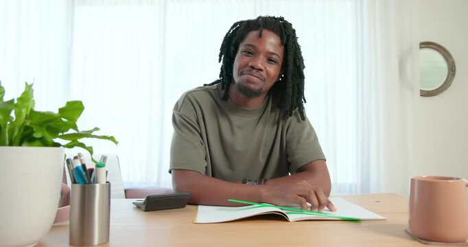 African American man flipping notebook pages, looking up and sharing ideas on camera at home table