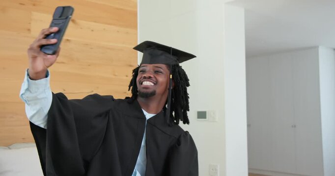African male wearing gown and cap, celebrating grad while recording selfies with smartphone at home
