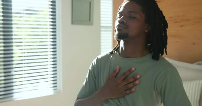 African American man responding to blinds, sitting up on bed and practicing slow breathing for calm