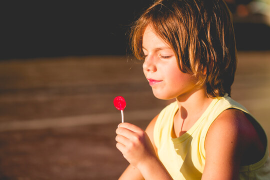 Close-up side view of a Boy in a vest sitting in the sun eating a lollipop