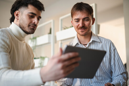 Two men collaborate on a digital tablet, discussing ideas in a modern office setting.
