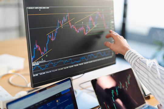 A person analyzes financial charts on a computer screen, with multiple devices displaying market data, indicating a focus on trading and investment strategies.