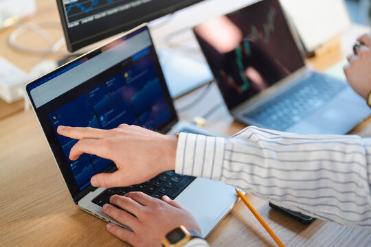 A person's hands interact with a laptop displaying financial charts and data, indicating analysis and trading activity.