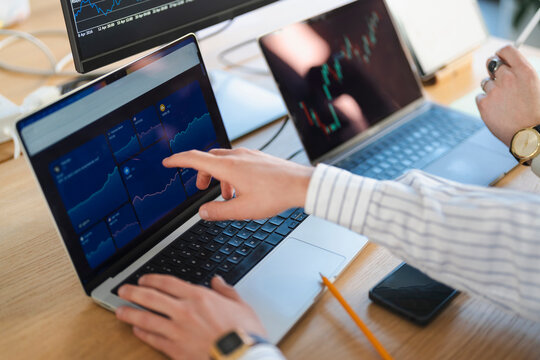 A person's hands are shown analyzing financial charts on multiple laptop screens, indicating a focus on trading and investment strategies.