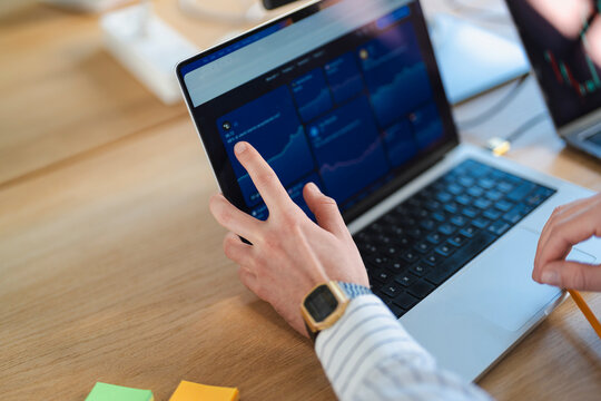 A person's hands are shown interacting with a laptop displaying financial charts and data, suggesting analysis or trading activity.