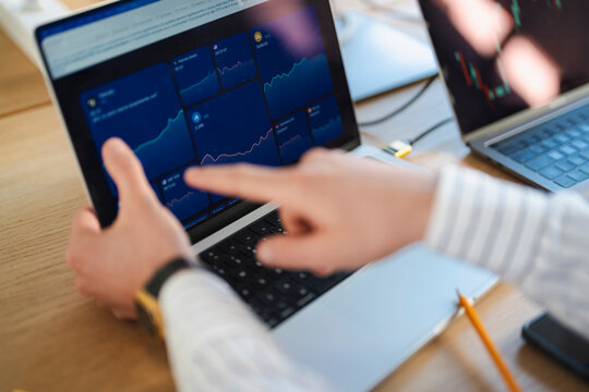 A person's hands interact with a laptop displaying financial charts and data, indicating analysis and trading activity.