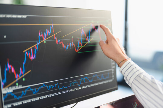 A person's hand points to a financial chart on a computer screen, analyzing market trends and data.