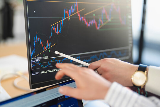 A person analyzes financial charts on a computer screen, using a stylus to point at the data.