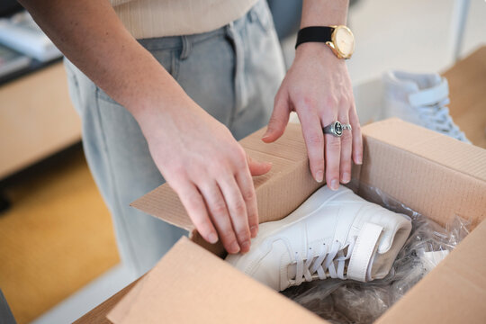 A person opens a cardboard box to reveal a new pair of white sneakers, ready for wear.
