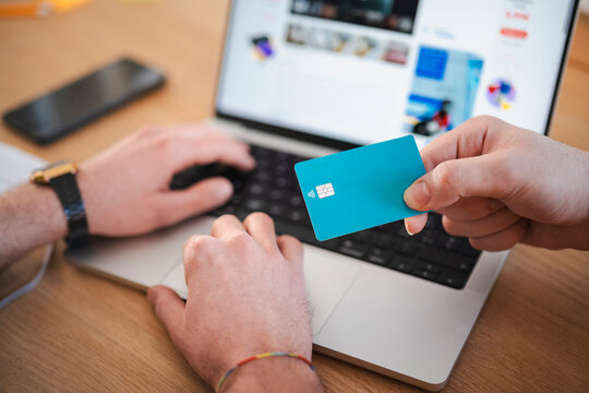 A person uses a laptop and holds a debit card, ready to make an online purchase.