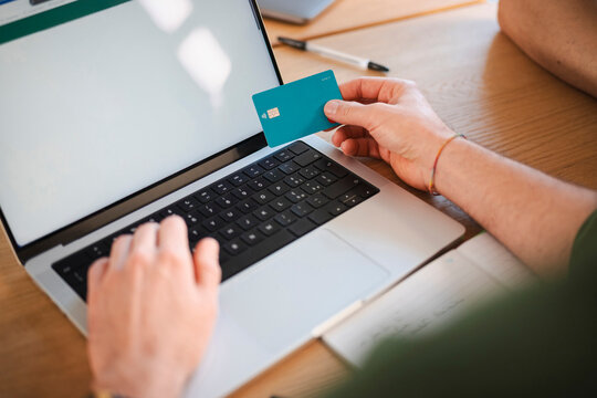 A person uses a debit card and a laptop to conduct online transactions, demonstrating digital commerce and financial management.