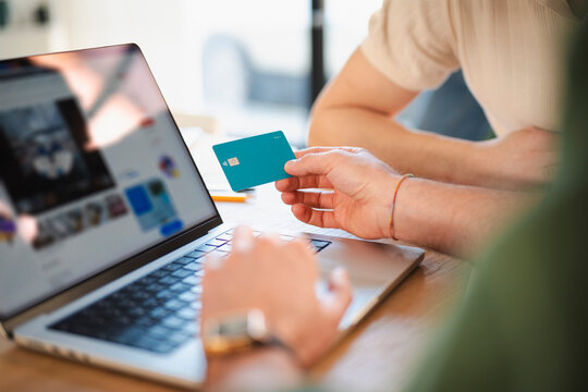 A person holds a debit card over a laptop, ready to make an online purchase.