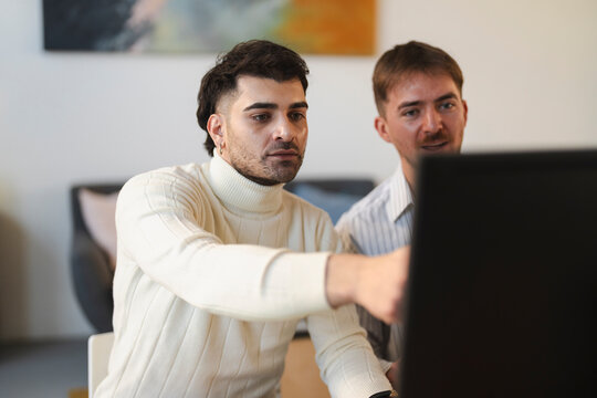 Two men collaborate on a project, one pointing at a computer screen while the other watches attentively.