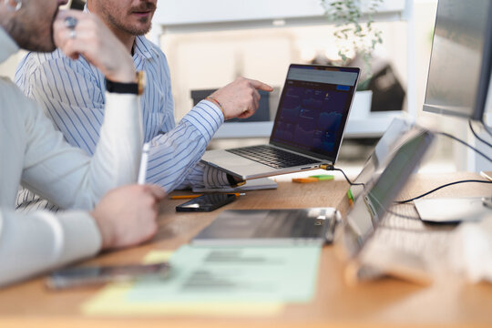 Two colleagues collaborate on a financial chart displayed on a laptop, discussing market trends and investment strategies in an office setting.