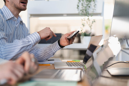 Two colleagues collaborate on a project, one pointing at a smartphone while the other uses a laptop in a modern office setting.
