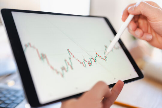 A person uses a stylus to interact with a financial chart displayed on a tablet, analyzing market trends and data.