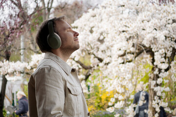 A man in headphones stands among spring blossoms, embodying calm technology that helps people reconnect with themselves. © Volha