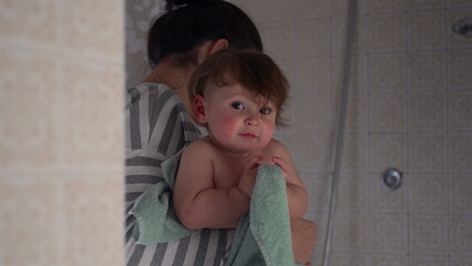 Fototapeta premium Baby chewing on towel while resting in mother’s arms after bath, intimate parenting moment of childhood curiosity, comfort, and gentle care at home