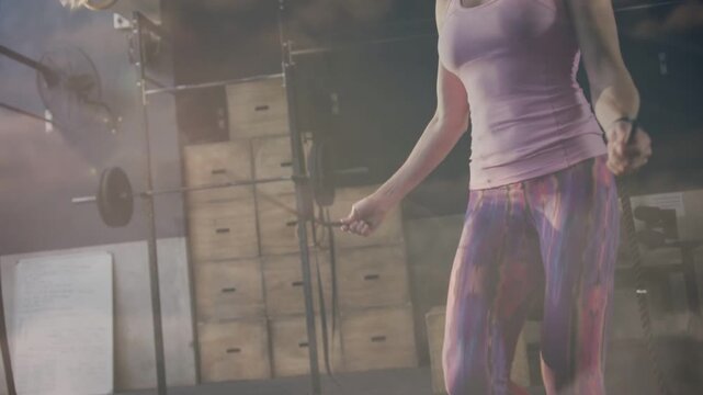 Female trainee skipping rope in gym training cardio, camera pulling back revealing rope arc, dust