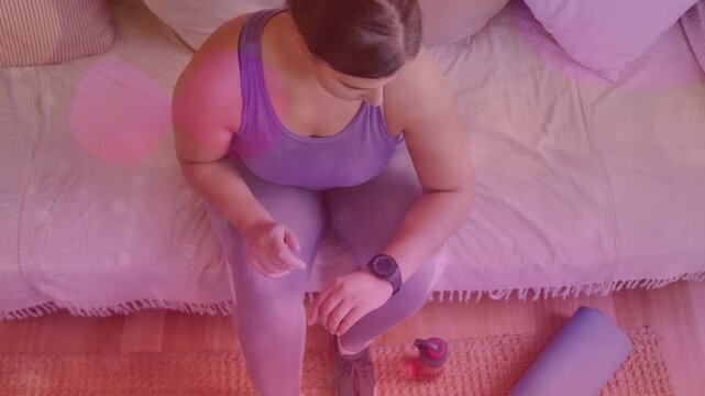 Woman leaning forward, tapping smartwatch and starting animated timer showing workout stats by mat