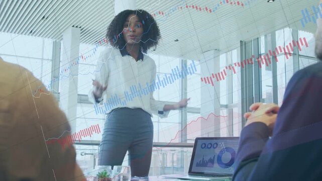 Female lead moving to table pointing at laptop charts biz overlays showing trends seeking consensus