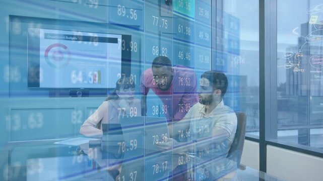 Standing man leaning over laptop causing seated duo typing and noting budgets as tickers moving