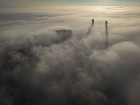 Aerial view of RWE Clauscentrale power plant with cooling towers and tall chimneys emerging through a thick layer of morning fog Maasbracht, Limburg, Netherlands.
