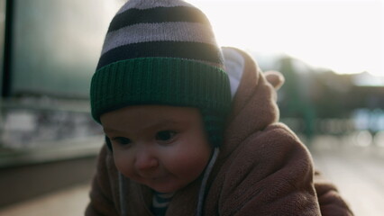 Baby in bear teddy fleece coat and striped beanie hat crawling forward outdoors, toddler exploring wooden surface with curious and playful energy during cold season © Marco