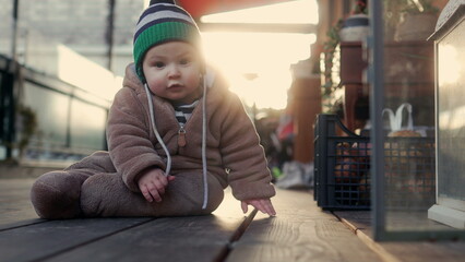 Baby crawling in bear teddy fleece coat and striped beanie hat outdoors on wooden floor, toddler exploring environment with curiosity during cozy winter family afternoon © Marco