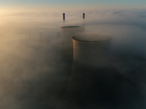 Aerial view of the RWE Clauscentrale power plant cooling towers and chimneys emerging from a thick layer of morning fog in Maasbracht, Limburg, Netherlands.