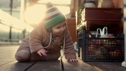 Baby crawling in bear teddy fleece coat and striped beanie hat smiling while moving on wooden floor, toddler exploring environment playfully during winter afternoon © Marco
