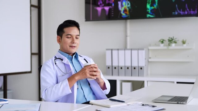 Professional doctor holding a hot coffee drink cup.doing paperwork checking medical documents at workplace. Concentrated physician reading medic form analyzing patient diagnosis or report in hospital.