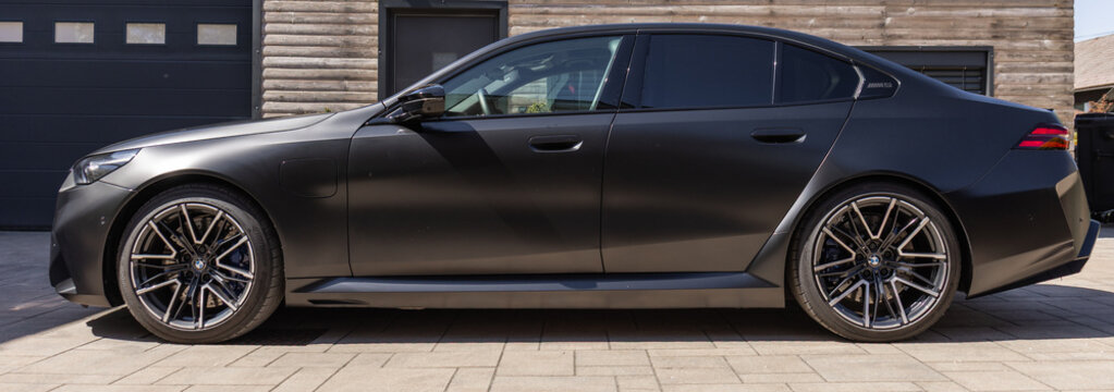 Slovenia, Ljubljana - 8 April 2026: BMW M5 is seen parked in front of a wooden structure on a sunny day.
