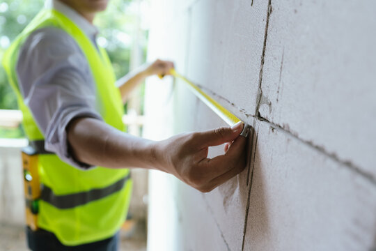Construction worker measuring a concrete wall with a tape measure at a building site, representing engineering, renovation, inspection, and construction work.
