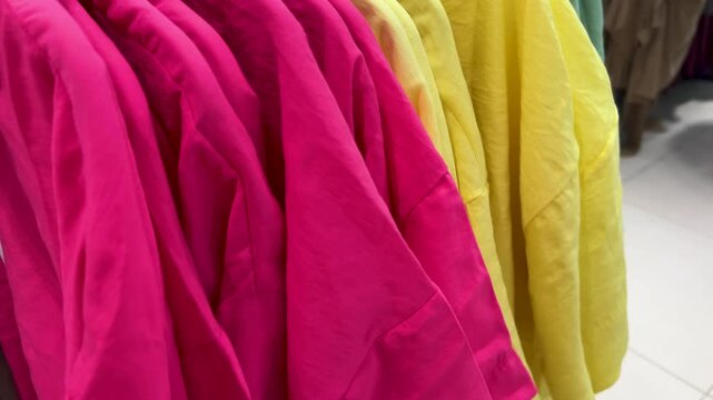 Horizontal 4K video. Pink shirt, yellow dress, green, blue clothes on hanger in clothing shop interior. Concept of Black Friday sale, 11 november, retail, promo, choice, buying textile thing, discount