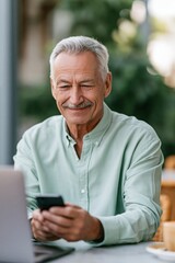 Obraz premium Senior man using smartphone with laptop at outdoor cafe