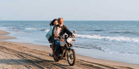Fototapeta premium Older couple riding motorcycle along shoreline on sandy beach