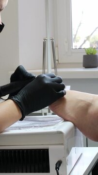 master Left-handed Technician uses electric pedicure foot file with interchangeable sanding abrasive heads to grind away rough skin on soles. Fine dead skin dust lifts off.