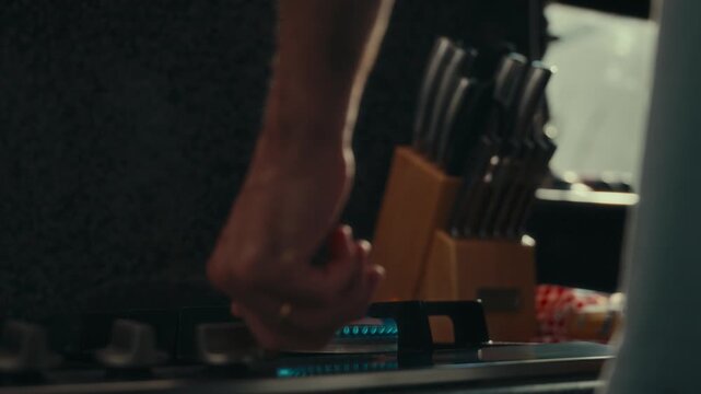 Close-up of hand turning stove knob. Knob twists, blue flame ignites under burner. Hand moves away from lit cooktop. Focused cooking action shot. Ideal for meal prep or kitchen scenes