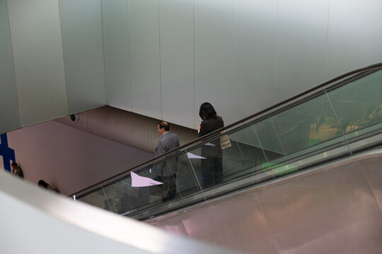 Two business silhouettes ascending an escalator in a modern corporate interior, rear view with clean lines and symmetry, conveying progress, mobility, and professional environment.