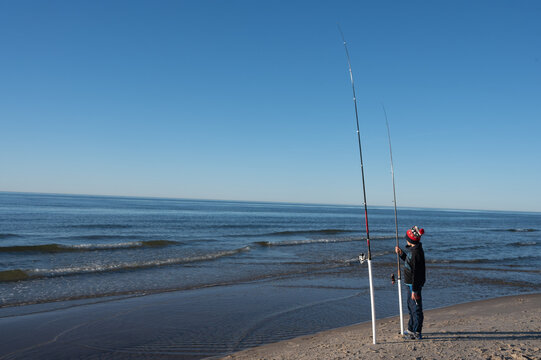 A child on the beach is fishing with two rods, using the beach fishing method. Surfcasting