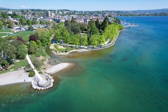 Aerial view of the lush green trees of Parc de l'Independance along the turquoise waters of Lake Geneva in Morges, Vaud, Switzerland.