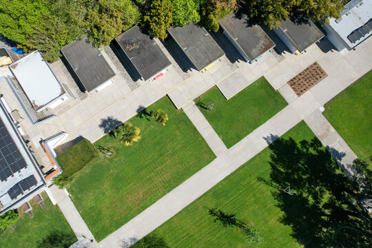 Aerial view of modern institutional buildings with flat roofs, solar panels, and concrete walkways crossing green lawns in Morges, Vaud, Switzerland.