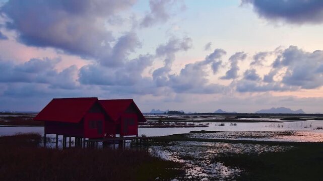 Timelapse Thale Noi Twin Wooden Shelters standing over reflective Phatthalung wetlands at sunrise, featuring iconic red-roofed stilt architecture and long Ekachai Bridge in rural Thailand.