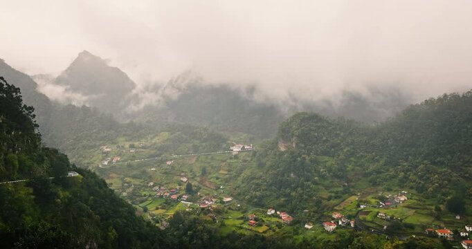 Aerial view of a village in a deep green valley surrounded by mountains covered in clouds and fog evergreen forest. Scenic landscape of Curral das Freiras in Madeira, Portugal.