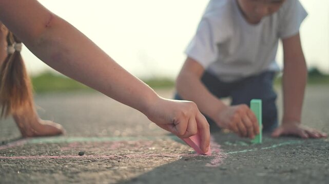 On the street, children and kids use hands and chalk for drawing art, playing together. Outdoor fun surrounds kids and children as chalk turns the street into colorful and happy outdoor art space.