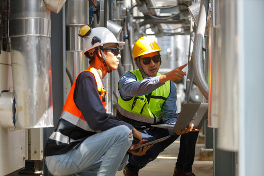 Two engineers in teamwork discuss hvac system piping on rooftop. They inspect industrial air cooling equipment for maintenance and quality control