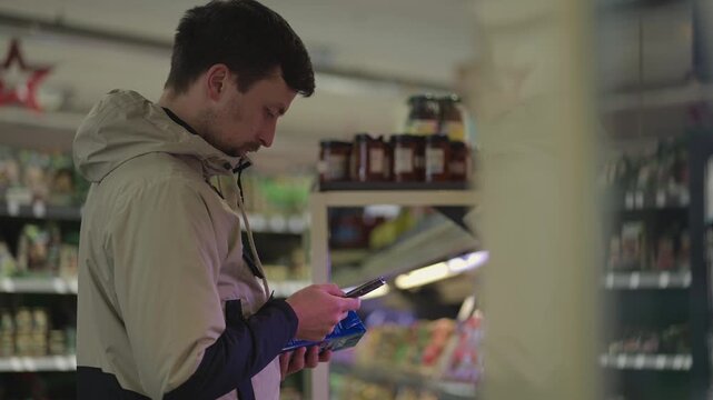 In grocery store aisle, man reviews his shopping list on smartphone and selects products from well stocked shelves. Scene everyday shopping, product comparison, and modern retail convenience.